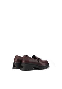 Scarpe in pelle bordeaux con punta rotonda, suola nera spessa e scanalata, e cinturino decorativo sulla parte superiore. Texture liscia, dettagli minimi.