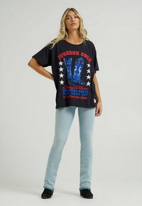 Camiseta negra de gran tamaño con un gráfico de botas de vaquero azules y texto rojo, combinada con jeans de un azul claro y botas negras de tacón.