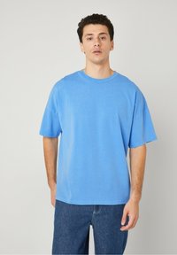 Modra bombažna majica s sproščenim krojem, kratkimi rokavi in okroglim ovratnikom. Gladka tekstura in enostaven dizajn. Usklajena z temnimi kavbojkami.