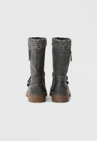 Bottes grises en cuir avec un revers tricoté gris et noir, des zips latéraux et une semelle texturée marron. Des sangles réglables sont sur le côté.