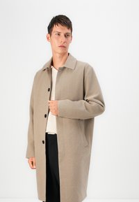 Beige wollen jas met een kraag, knopen vooraan en zijzakken. Zachte textuur, rechte snit en minimalistisch ontwerp.