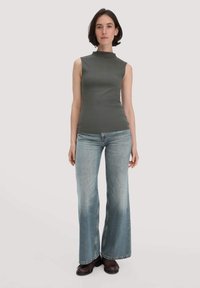 Graues ärmelloses Oberteil mit hohem Ausschnitt, kombiniert mit weit geschnittenen, hellblauen Jeans und dunklen Schuhen. Glatte Textur und taillierte Passform.