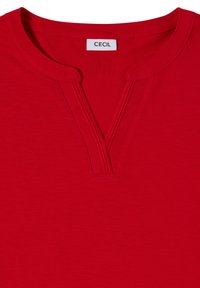 Chemise rouge avec un col en V fendu et une étiquette de marque blanche indiquant "CECIL" cousue à l’intérieur de l’encolure.