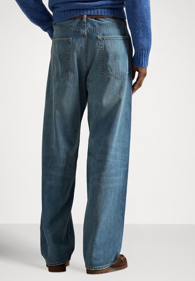 Τζιν παντελόνι με φαρδύ πόδι σε ανοιχτό μπλε χρώμα, με ξεθωριασμένη υφή, δύο πίσω τσέπες και ορατές ραφές. Φορεμένο με καφέ casual παπούτσια.