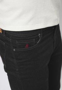Zwarte denim jeans met een slim fit, voorzien van een rood geborduurd logo op de voorzak en standaard metalen accenten.