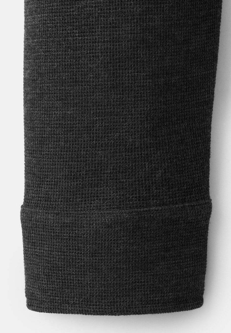 Schwarzer Waffelstrickstoff mit strukturierter Oberfläche und einem anliegenden Bündchen am unteren Rand. Der Stoff wirkt weich und langlebig.