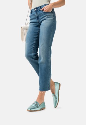 Et par lyseblå metallic loafers med flad sål og dekorativ hardware, båret med medium vaskede lige ben jeans med frynset kant.