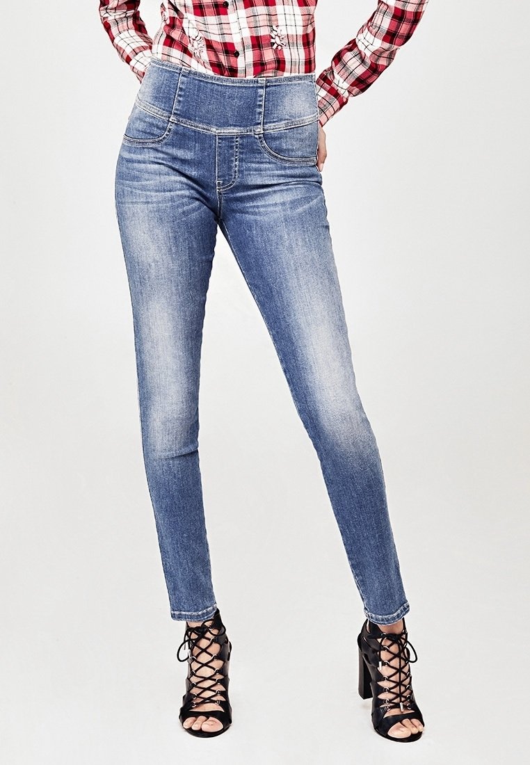 Jean bleu taille haute avec un effet délavé, design à cinq poches et détails cousus, associé à des sandales à talons hauts noires avec lanières.