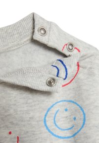 Grauer Pullover mit geripptem Halsausschnitt und Druckknöpfen. Verfügt über bunte Smiley-Gesichtsmuster in Blau und Rot auf dem Stoff. Weicher Griff.