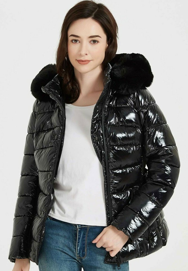 Doudoune noire avec finition brillante, capuche en fausse fourrure, design matelassé, fermeture éclair à l'avant et fermeture à pression. Portée par-dessus un haut blanc.