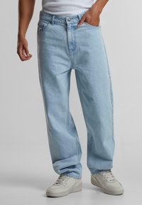 Blugi din denim de culoare albastru deschis, cu o croială lejeră, având buzunare frontale, închidere cu un singur buton și accente de cusătură. Asortați cu adidași deschiși.