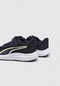Scarpe da ginnastica nere con un upper testurizzato, suola bianca e una striscia verde acentuata; presentano una cinghia in velcro per una chiusura sicura.
