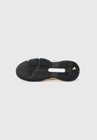 Zwarte rubberen zool van sportieve schoen met zigzagprofiel en klein groen driehoekig logo op witte achtergrond.