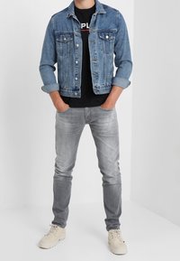 Jeansjacka i ljusblått, lång ärm, två framfickor. Svart t-shirt med logotyp under. Slim fit grå jeans och beige sneakers.