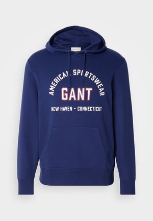 Marineblå hættetrøje med snøre i hætten, frontlomme og fed hvid og rød tekst, der står "GANT AMERICAN SPORTSWEAR NEW HAVEN - CONNECTICUT."