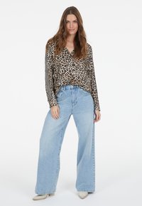 Leopard print long-sleeve blouse with button-down collar, paired with wide-leg light blue jeans. The outfit is completed with beige footwear.