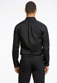 Zwarte langgaande blouse met een klassieke kraag, een soepele textuur, een plooidetail aan de achterkant en met knoopmanchetten, gecombineerd met zwarte broek.