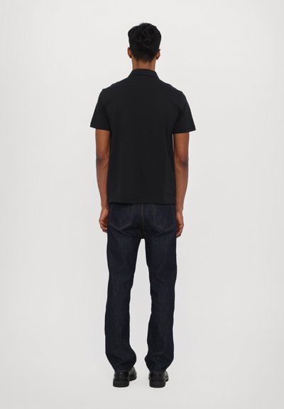 Polo preto com mangas curtas, apresentando um colarinho clássico. Combinado com jeans de ganga azul escuro. Design simples, sem padrões visíveis.