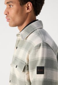 Geruite flanellen shirt in lichtgroen en crème, met een knoopsluiting aan de voorkant, een borstzak en een gestructureerde stof met een merkpatch op de mouw.