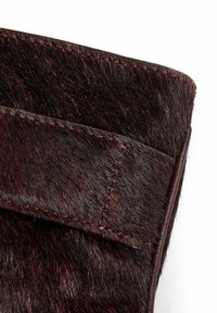 Tumši brūns matēta āda ar gludu ādas apdari. Satur kontrastējošu stitching un taisnstūra formu ar noapaļotām malām.