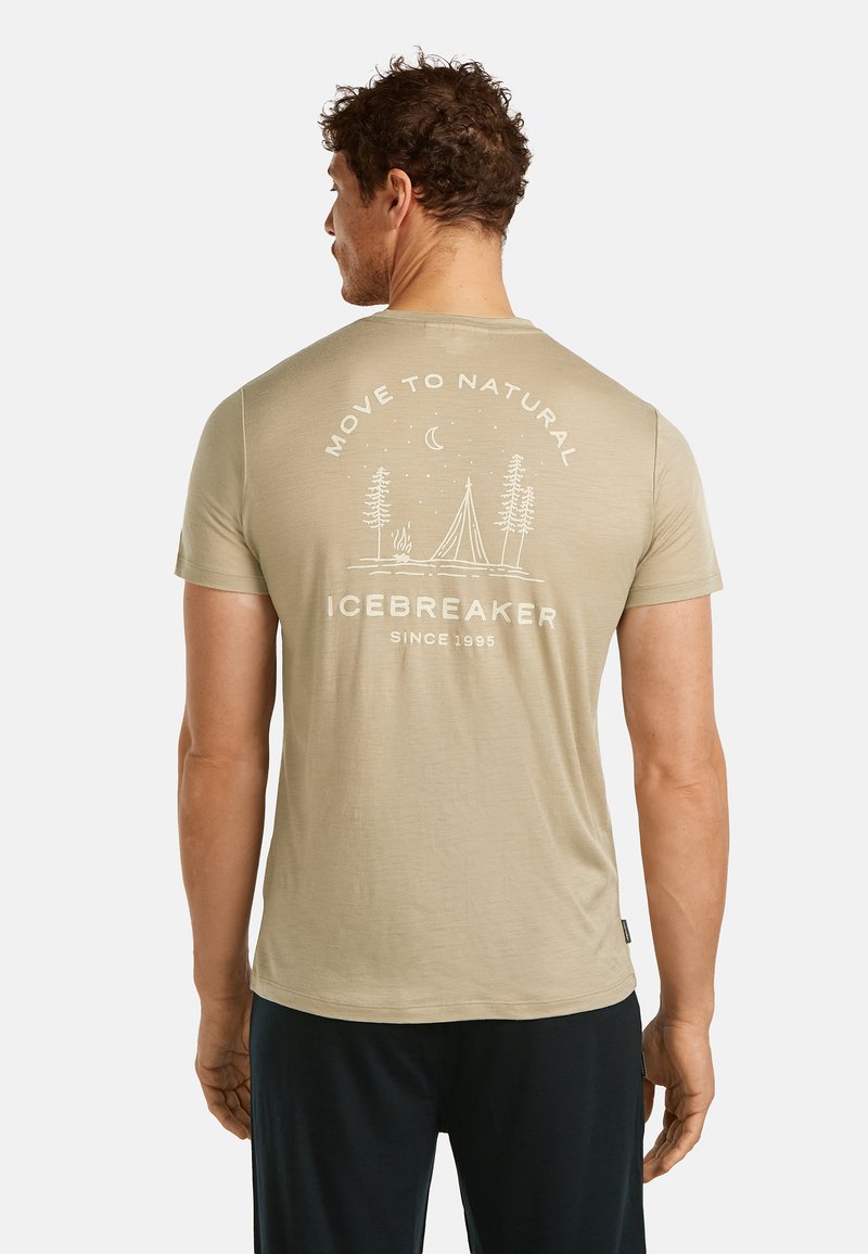 Mann trägt ein beiges T-Shirt mit der Aufschrift "Move to Natural Icebreaker Since 1995" und einem Camping-Szenenmotiv, steht mit dem Rücken zur Kamera.