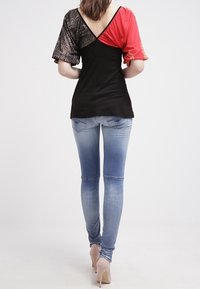 Blusa negra y roja con diseños de mangas variados; cuerpo negro con tela roja y estampada en las mangas; combinada con jeans ajustados azules y tacones nude.