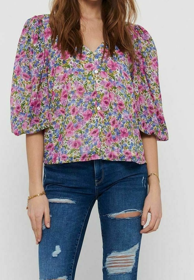 Blumenbluse in Lila und Grün, mit Puffärmeln, V-Ausschnitt und Knopfverschluss. Kombiniert mit dunkelblauen, ausgebleichten Jeans.