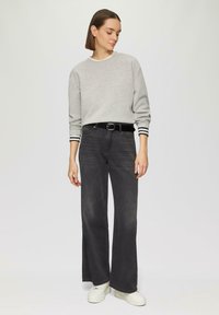Sweatshirt gris avec des poignets à rayures noires et blanches, associé à un jean foncé taille haute et des baskets plateformes blanches. Design simple et coupe décontractée.