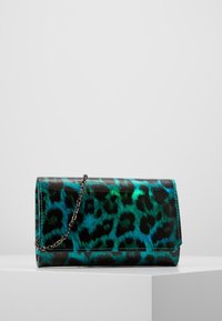 Piccola borsa a pochette rettangolare con stampa leopardata metallizzata turchese e nera e una sottile tracolla in argento, posizionata su un piedistallo bianco.