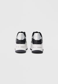 Must nagu ja hõbedased platvormi tossud, millel on voolujooneline disain, tekstuuriga materjal, paks valge tald ja logo aktsendid kandadel.