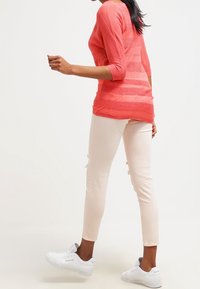 Sweter w paski w odcieniach koralu z rękawami do trzech czwarte, zestawiony z jasnoróżowymi, przetartymi skinny jeansami i białymi trampkami, prezentujący casualowy strój.