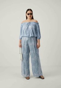 Ανοιχτό μπλε τοπ off-the-shoulder με κορδόνι και φουσκωτά μανίκια, συνδυασμένο με παντελόνι wide-leg από παρόμοιο ύφασμα; αξεσουάρ με μαύρα γυαλιά ηλίου και λευκή τσάντα.