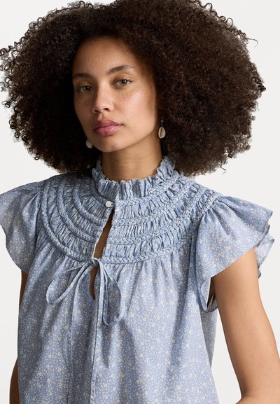 Lichtblauwe blouse met een gesmokt decolleté, rimpelige korte mouwen, bloemenpatroon en een sleutelgatopening aan de voorkant die met een strik is vastgemaakt.