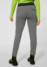 Black and white houndstooth patterned trousers with a fitted shape, elastic waistband, and side pockets, paired with black ankle boots.