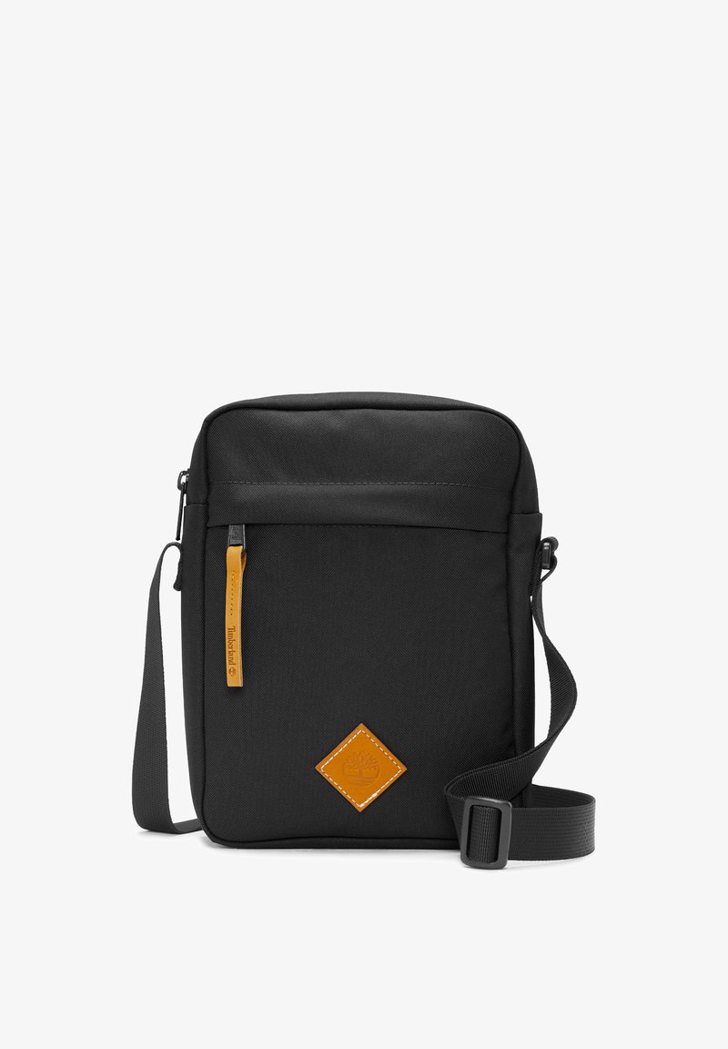 Černá látková taška přes rameno, obdélníkový tvar, s přední zipovou kapsou, oranžovým koženým detailem a nastavitelným popruhem.