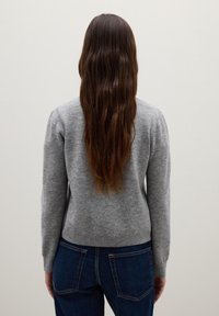 Maglione grigio lavorato a maglia con maniche lunghe, design aderente e orlo a costine. Indossato con jeans in denim blu, che mostrano un aspetto rilassato e casual visto da dietro.