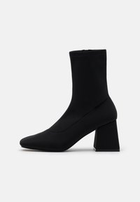 Bottines noires en tissu extensible avec un bout pointu et un talon carré. Le design est élégant, avec des coutures invisibles et une texture lisse.