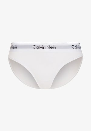 Bílé bavlněné bikiny s elastickým páskem v černé a šedé barvě se vzorem "Calvin Klein" podél vršku. Hladká textura a minimalistický design.