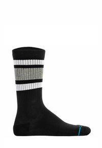 Calcetín negro con textura acanalada, que presenta rayas horizontales en gris y blanco. Un pequeño detalle en turquesa está cerca de la zona del dedo del pie.