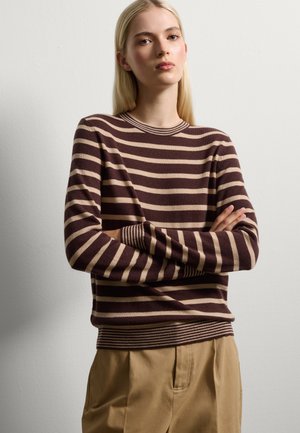 Pull rayé marron et beige avec un col rond et des poignets côtelés, associé à un pantalon en tissu beige. Texture lisse et coupe décontractée.