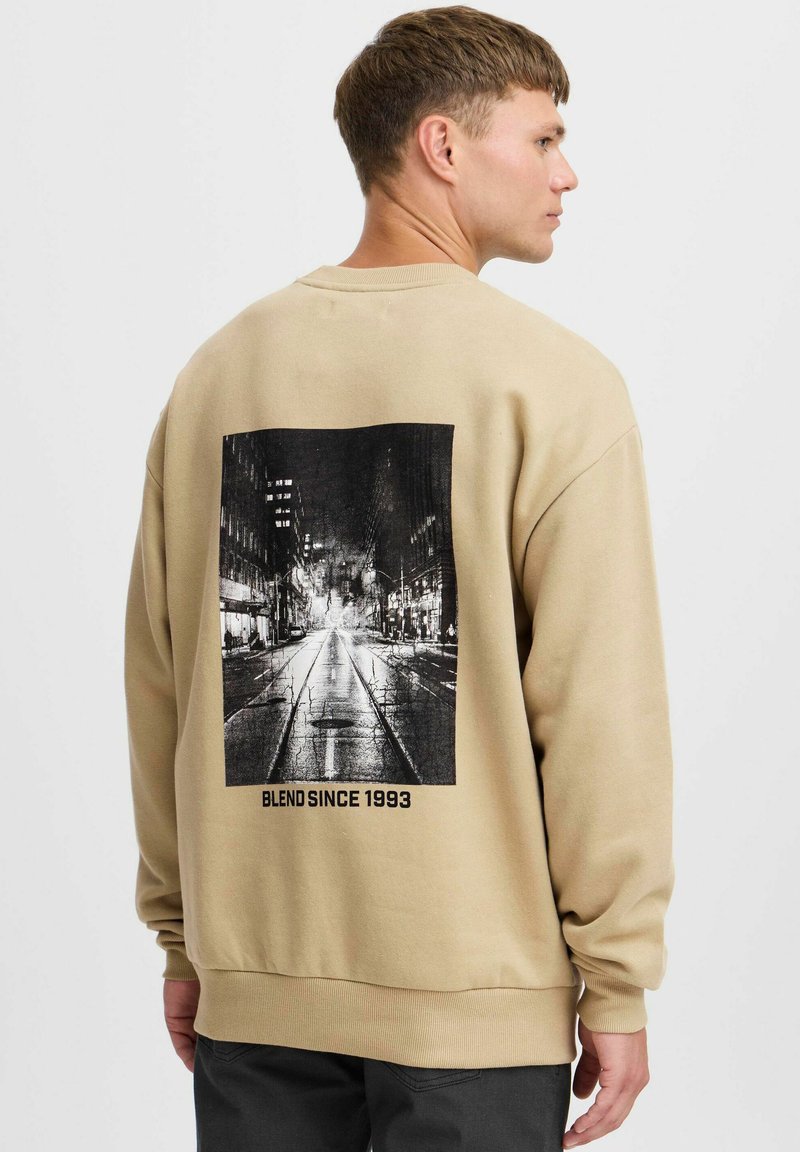Beige sweatshirt met een zwarte grafische afbeelding van een stedelijke straatscene op de achterkant, met de tekst "BLEND SINCE 1993" eronder.