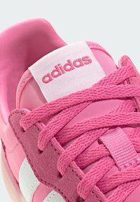 Ružičasta sportska cipela s glatkim tkaninskim tijelom, antilop naglascima, teksturiranim vezicama i bijelom crtom, s oznakom "adidas" na jeziku.