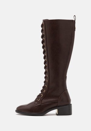 Botte haute en cuir marron foncé avec lacets à l'avant, œillets dorés, bout arrondi, petit talon bloc et languette à l'arrière.