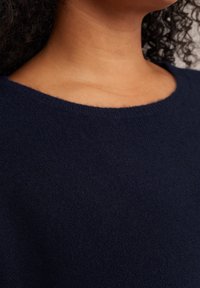 Pulover tricotat de culoare albastru marin cu guler rotund, având o suprafață moale și texturată, cu o ușoară elasticitate. Țesătura pare călduroasă și primitoare.