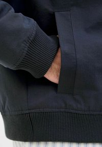 Černá bomber bunda s žebrovanými manžetami a pasem, hladká textilie, boční kapsa a čistý, moderní silueta.