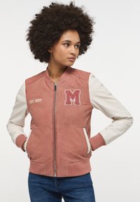 Różowa zamszowa bomberka z kremowymi rękawami, ozdobiona haftowaną literą "M" i tekstem "EST. 1932", z ribbowanymi mankietami i bocznymi kieszeniami.