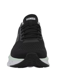 Chaussure de sport noire avec une tige en maille, présentant des accents gris, des lacets noirs et une semelle intermédiaire vert menthe. Semelle extérieure en caoutchouc texturé pour une adhérence optimale.