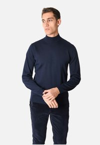 Maglione a collo alto blu navy in un morbido e liscio tessuto a maglia, con maniche lunghe e orlo a coste. Abbinato a pantaloni di velluto a coste scuri.