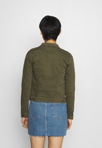 Olivgrüne Jeansjacke mit strukturierter Passform, Knopfdetails an den Manschetten und klassischem Kragen, kombiniert mit einem hellblauen Jeansrock.