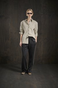 Camicia a scacchi marrone chiaro con chiusura a bottoni, abbinata a pantaloni neri a sigaretta con piping bianco sui lati. Scarpa marrone.